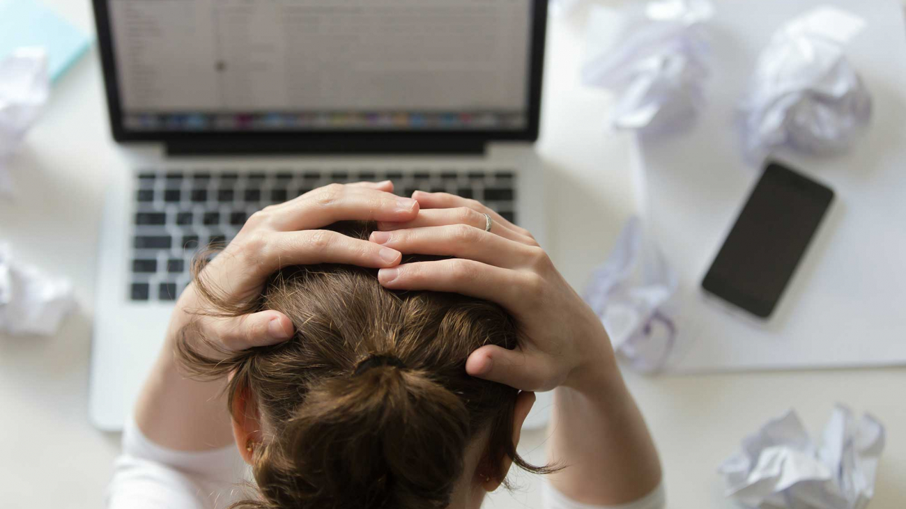 The Cost Of Stagnation_portrait-woman-grabbing-head-desk-near-laptop